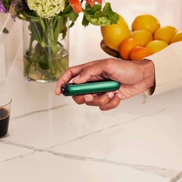 Uma mão a segurar o dispositivo Ploom AURA com um painel frontal Amazon Green.
