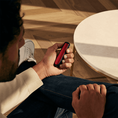 Uma mão a segurar o dispositivo Ploom AURA com um painel frontal Lava Red. 