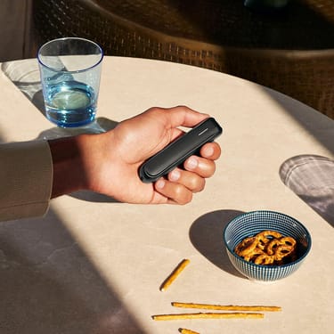 Uma mão a segurar o dispositivo Ploom AURA com um painel frontal Jet Black.