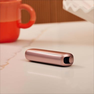 Plano aproximado de um painel frontal Rose Gold para Ploom AURA numa superfície plana.