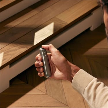 Uma mão a segurar o dispositivo Ploom AURA com um painel frontal Lunar Silver.